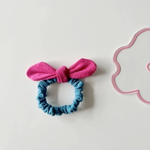 Detail view of a pink and blue suede bow hair tie on a minimalist white background