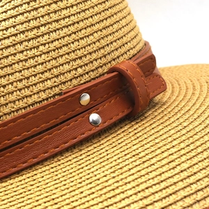 Detailed macro view of woven straw hat featuring brown leather band and silver rivets