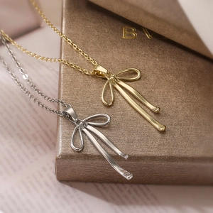 Minimalist gold and silver bowknot tassel necklaces on a metallic jewelry box