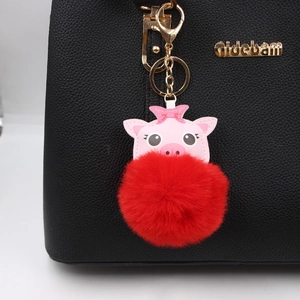 Cute pink pig plush keychain with red fluffy pompom on a black leather handbag