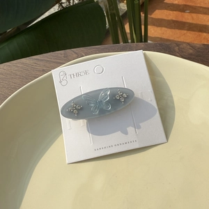 Detail of blue-grey oval acetate hair clip with transparent butterfly and rhinestones