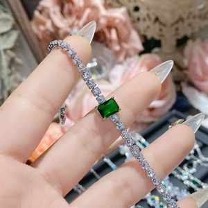 Detailed macro view of an emerald-cut green gemstone on a diamond-paved silver bracelet