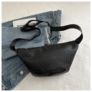 Close-up of black woven leather chest bag with adjustable strap on denim background