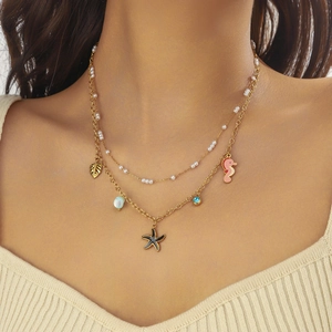 Detail of layered gold necklace featuring pearl, leaf, starfish and seahorse pendants