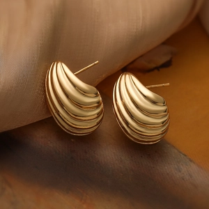 Elegant gold-plated spiral shell-textured teardrop stud earrings on champagne silk