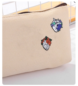 Detail of anatomical heart enamel pins with floral designs pinned on a beige canvas bag