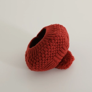 Vue détaillée du béret tricoté rouge avec un grand pompon et une texture de laine épaisse