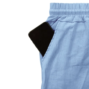 Détail d'une grande poche latérale sur un pantalon en lin bleu clair avec smartphone