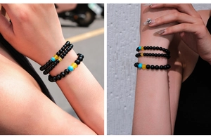 Detail of stacked black agate beaded bracelets with blue and yellow accent beads on a wrist