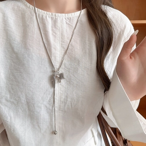 Model wearing a silver Y-chain necklace with a sleek pony tassel pendant on white clothing