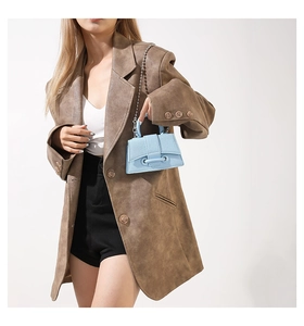 Detail of light blue mini leather handbag with silver chain strap on a brown blazer