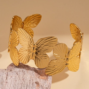 Macro detail of gold-plated butterfly pattern on a textured metal open cuff bracelet