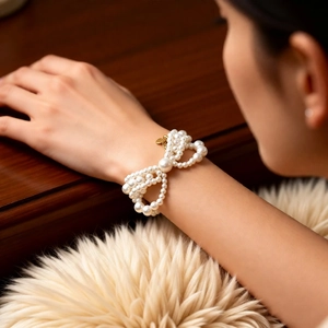 Close-up of pearl bracelet with golden bow pendant on a soft white plush background