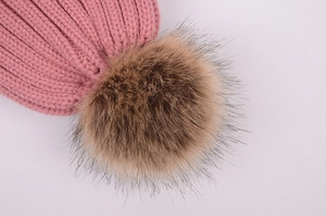 Detail view of pink knitted beanie featuring a large brown faux fur pom pom decoration