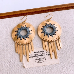 Detail of bohemian gold hollow round earrings with dark grey tassels and woven thread