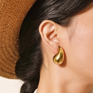 Close-up of woman wearing large polished gold teardrop earrings in a summer setting
