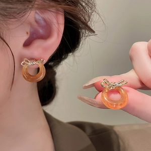 Macro shot of gold bow knot earrings with amber resin hoop detail on female model