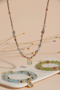 Close-up of peridot and aquamarine beaded jewelry set with gold pendants on a tray