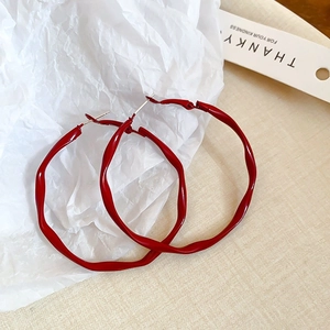 Detail showing red hoop earrings with irregular wave texture and glossy finish