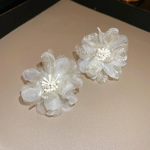 Close-up of delicate mesh flower earrings with pearl centers on leather background