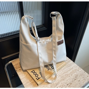 Detail of white canvas tote bag showing fashion logo plaque and side pocket storage