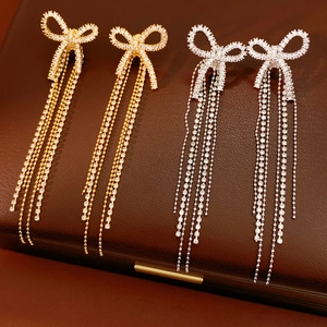 Detail of 18k gold plated bow earrings with long sparkling tassels on leather background