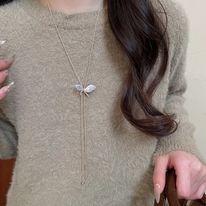 Detail of a golden butterfly pendant necklace with pearls on a brown sweater background
