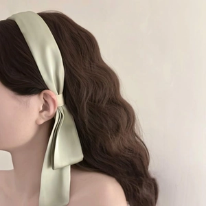 Detail of light green satin bow hair ribbon styled on brown wavy hair for a soft elegant look