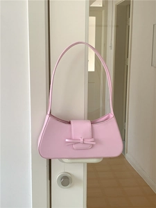 Pink faux leather baguette shoulder bag with decorative bow hanging on a white handle