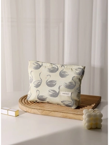 Elegant swan jacquard makeup bag in cream canvas with red beak detail on a wooden tray