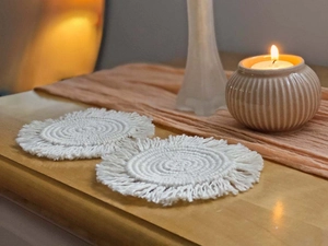 Detail showing two handmade round woven cotton coasters with tassels on a wooden table
