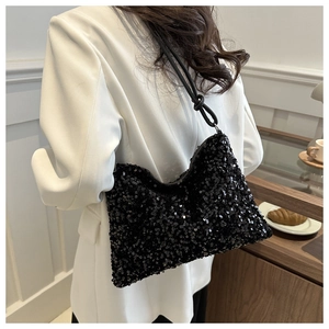 Détail d'un sac à bandoulière noir à paillettes porté avec un blazer blanc élégant