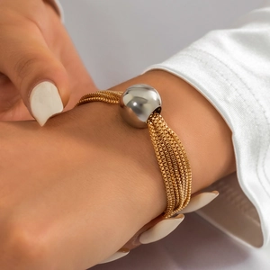 Close-up of layered gold chain bracelet with a large silver spherical bead detail
