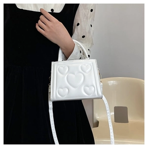 Gros plan d'un sac à bandoulière blanc avec motifs de cœurs gaufrés et texture brillante