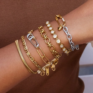 Close-up of layered paperclip and tennis bracelets with heart charms in gold and silver finish