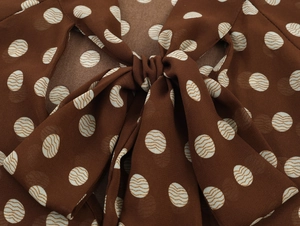 Gros plan d'une blouse en mousseline marron à pois blancs avec un nœud élégant au col