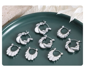 Detail of silver twist texture hoop earrings and seashell pattern studs in a green tray