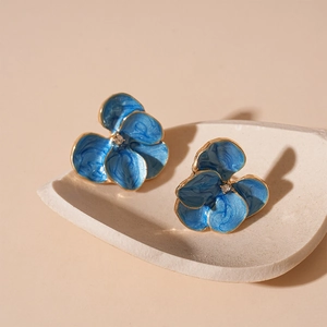 Elegant blue enamel flower earrings with gold edges and small crystals on a white tray