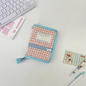 Close-up of pink checkered quilted binder cover with blue zipper and brand label on desk