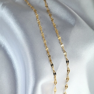 Detailed close-up of a gold-plated titanium steel necklace chain on white silk fabric