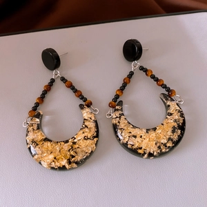 Macro detail of crescent resin earrings featuring gold foil flakes and black beads