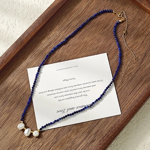 Deep blue beaded necklace with white pearls and gold clasp on a wooden background