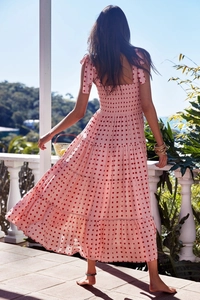 Back view of pink tiered gingham sundress with smocked bodice and tie-straps in outdoor setting