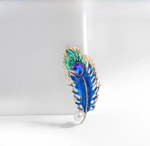 Macro shot of peacock feather brooch with blue enamel, rhinestones, and white pearl detail