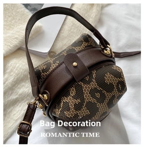Detail of leopard print cylinder bag with leather trim and gold hardware on soft bedding