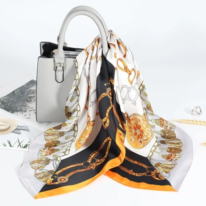 Dettaglio di un foulard in seta stampata con motivo a catena legato a una borsa grigia