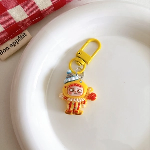 Detailed view of a cute cartoon clown keychain charm with yellow D-ring on white ceramic tray