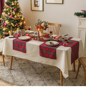Detail of red and green plaid table runner on beige linen cloth with festive Christmas setting