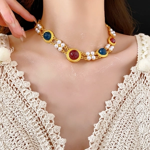 Close-up of vintage gold necklace with pearls and colorful gemstones worn by a model