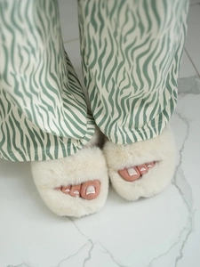Close-up of white plush faux fur slippers paired with mint green striped pajama pants